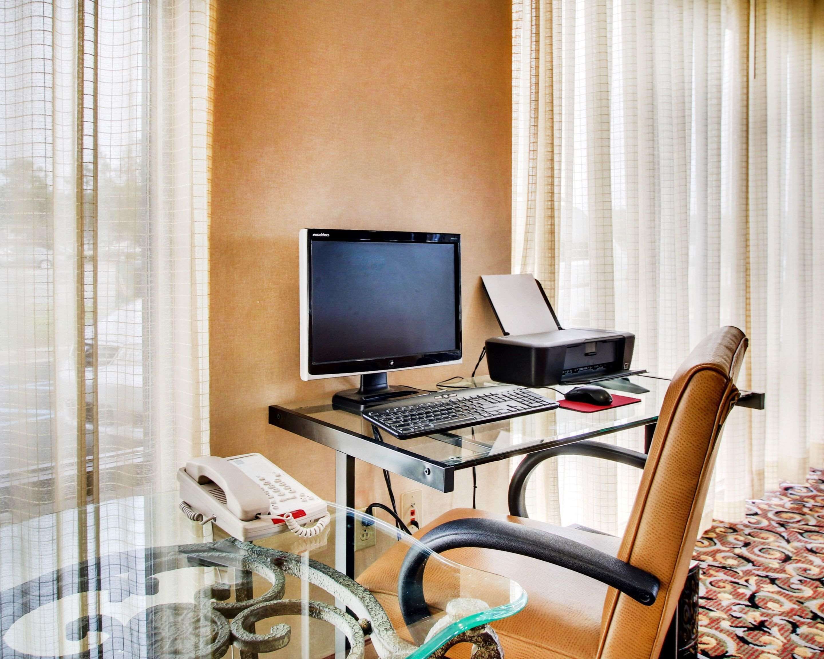 Une chambre d’hôtel équipée d’un bureau en verre, d’un ordinateur, d’une imprimante, d’un téléphone et d’une chaise.
