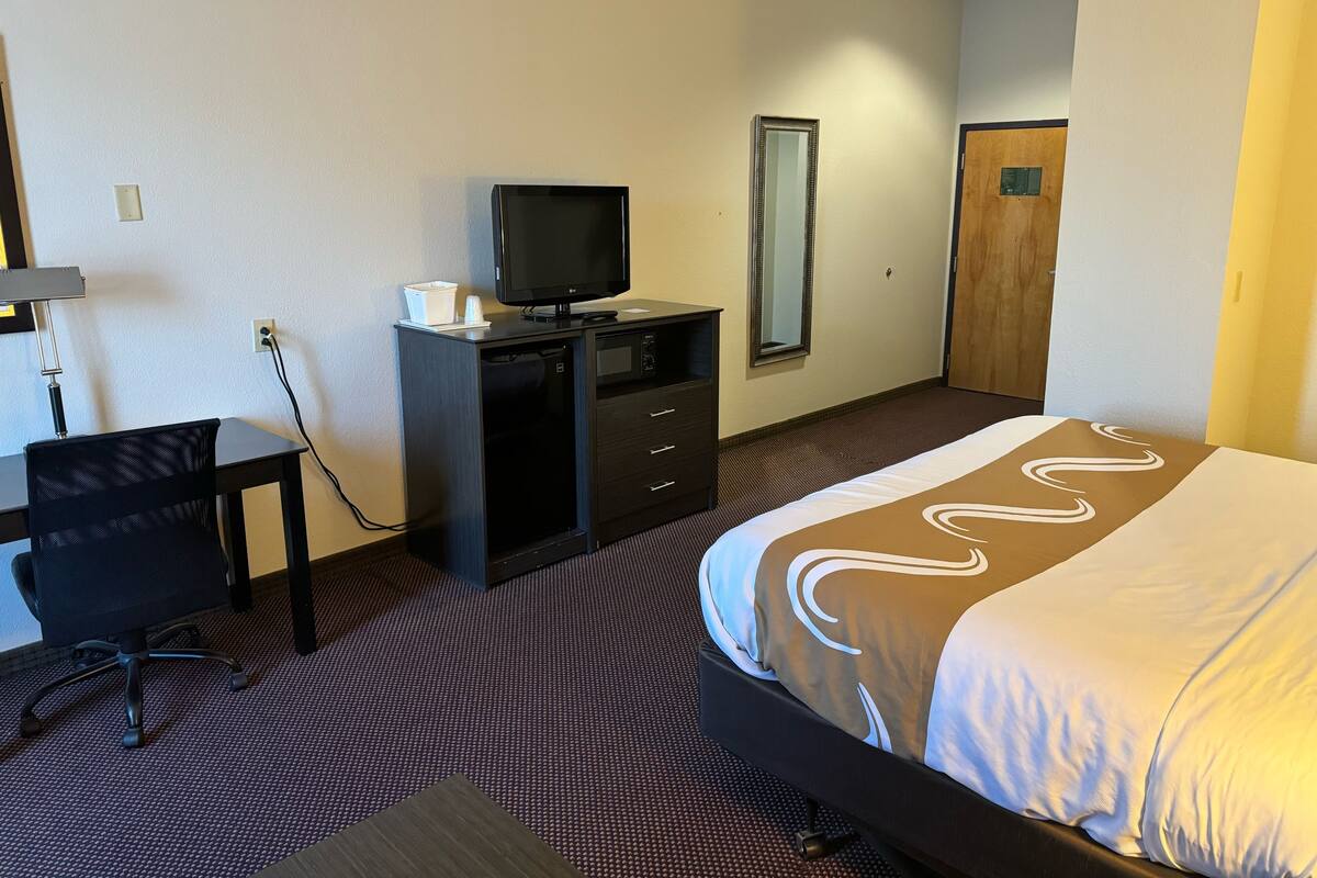 Een hotelkamer met een bed, een bureau, een televisie en een kledingkast.