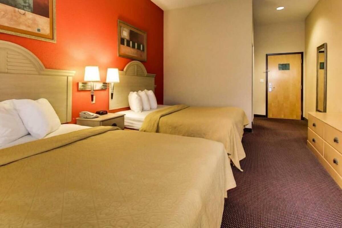 Hotelkamer met twee bedden, een hoofdeinde, nachtlampjes, een telefoon en een deur naar een andere kamer.