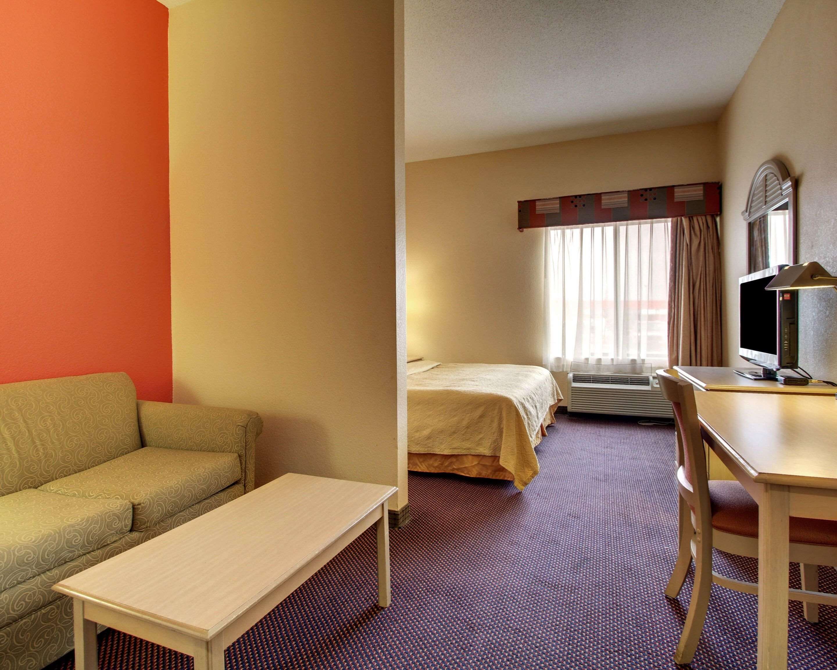 Habitación de hotel con cama, escritorio con computadora, una mesita y un sofá.