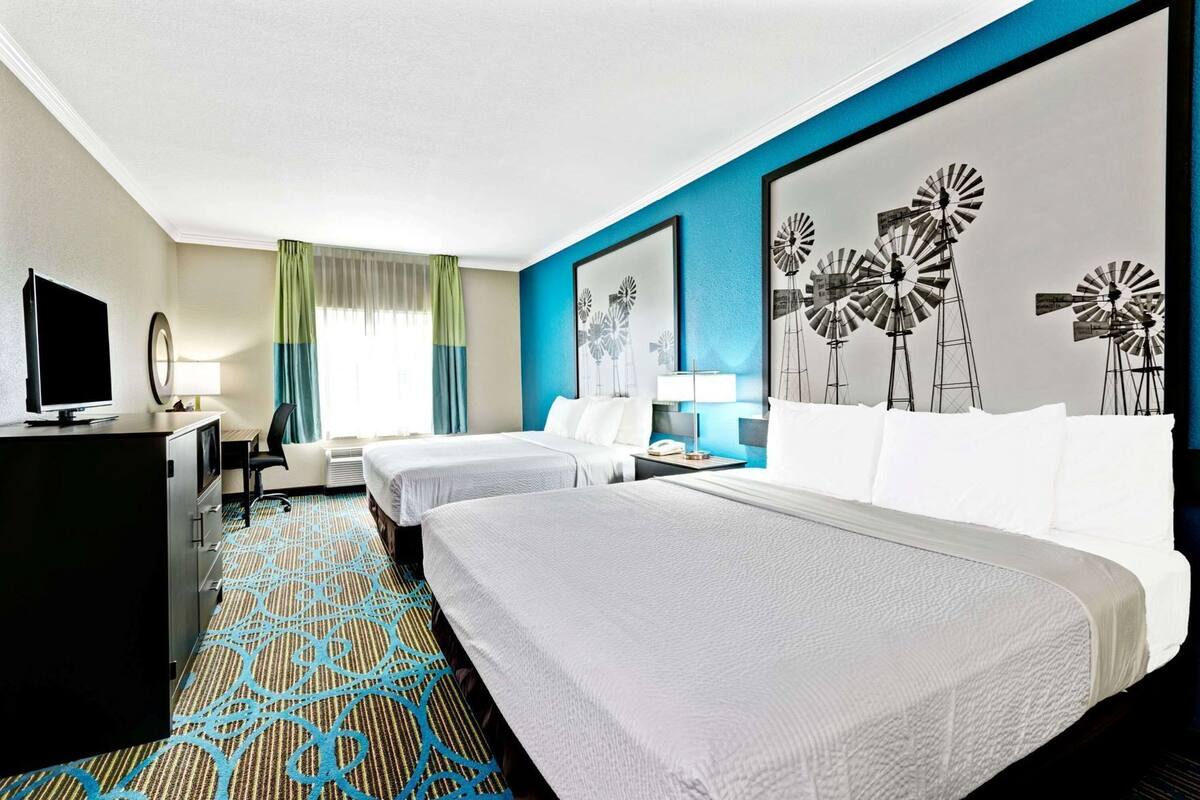 Ein Hotelzimmer mit zwei Betten, einem Schreibtisch, einem Fernseher und einem großen Wandbild.