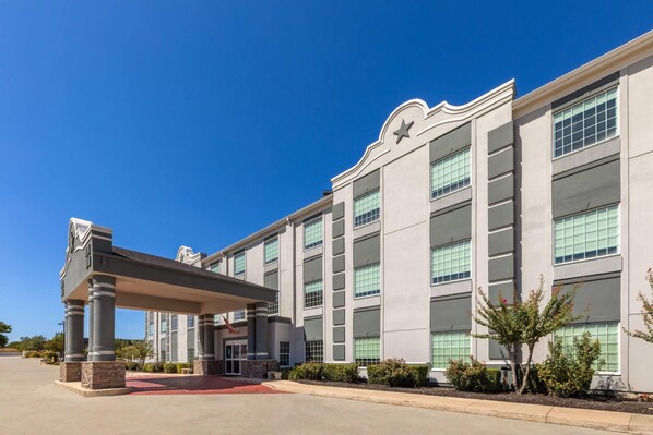 A modern hotel with a covered entrance, large windows, and a star on the facade. - Super 8 by Wyndham San Antonio/Alamodome Area (San Antonio)