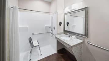 Une salle de bain adaptée aux personnes handicapées, équipée d’une douche, de barres d’appui, d’un fauteuil roulant et d’un lavabo avec un plan de travail en granit.