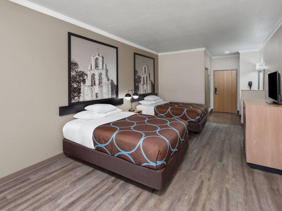 A hotel room with two beds, a wooden desk, a television, and framed pictures on the wall.