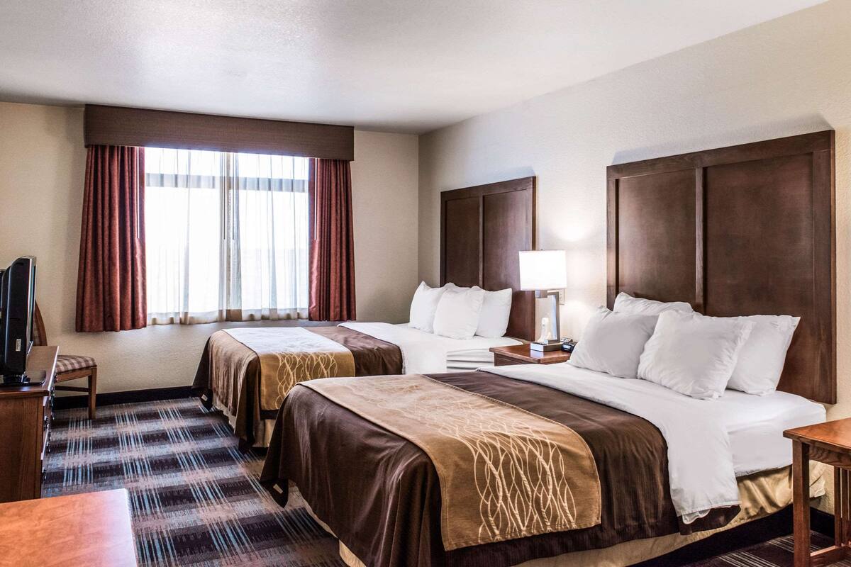 Habitación de hotel con dos camas, un escritorio, una silla, un televisor y una ventana con cortinas.