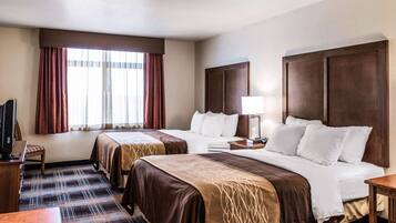 A hotel room with two beds, a desk, a chair, a TV, and a window with curtains.