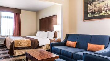 Una habitación de hotel con cama, sofá, mesa de centro y un cuadro en la pared.
