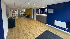 Een receptiegedeelte met een blauwe muur, een receptiebalie en een bord met daarop de kantoor van de algemeen directeur.