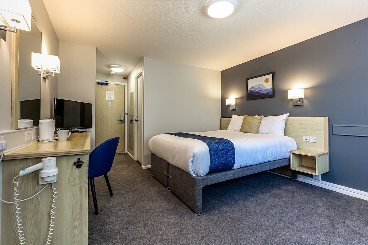 Ein Hotelzimmer mit Bett, Schreibtisch mit Computer, Spiegel und Wandlampe.