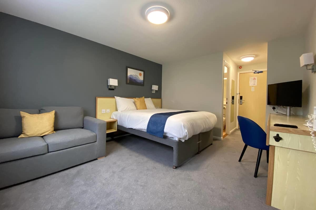 Ein Hotelzimmer mit Bett, Sofa, Schreibtisch und Fernseher.