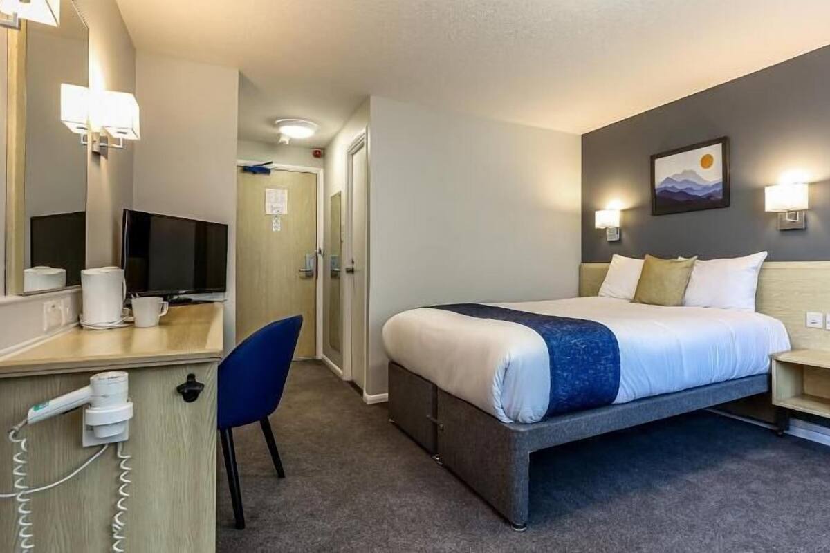 Ein Hotelzimmer mit Bett, Nachttisch, Schreibtisch mit Stuhl, Fernseher und Spiegel.