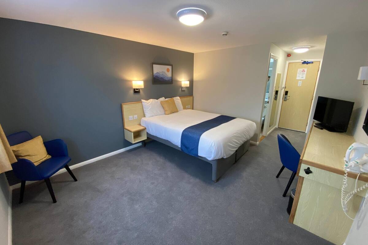 Ein Hotelzimmer mit Bett, Nachttischen, einem Schreibtisch mit Telefon, einem Sessel und einem Fernseher.