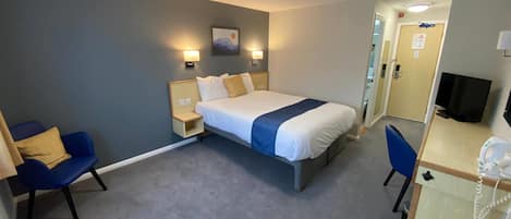 A hotel room with a bed, bedside tables, a desk with a telephone, a chair, and a television.