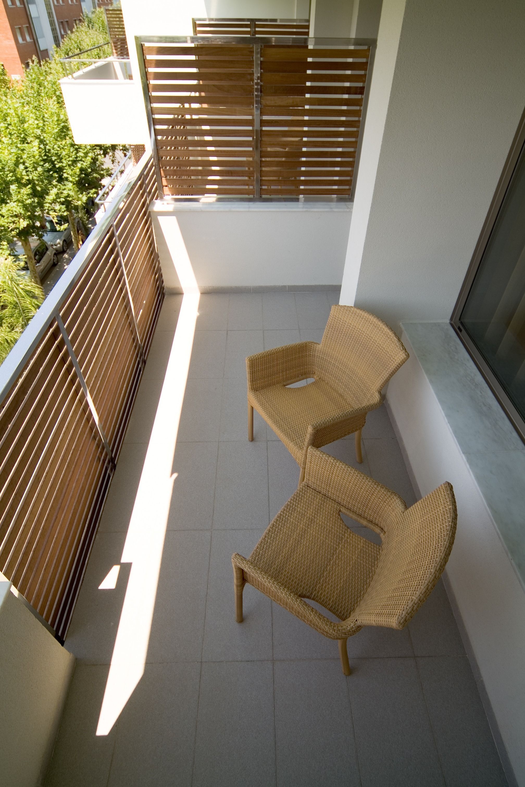 A balcony with two wicker chairs, a metal railing, and a view of a building in the background.