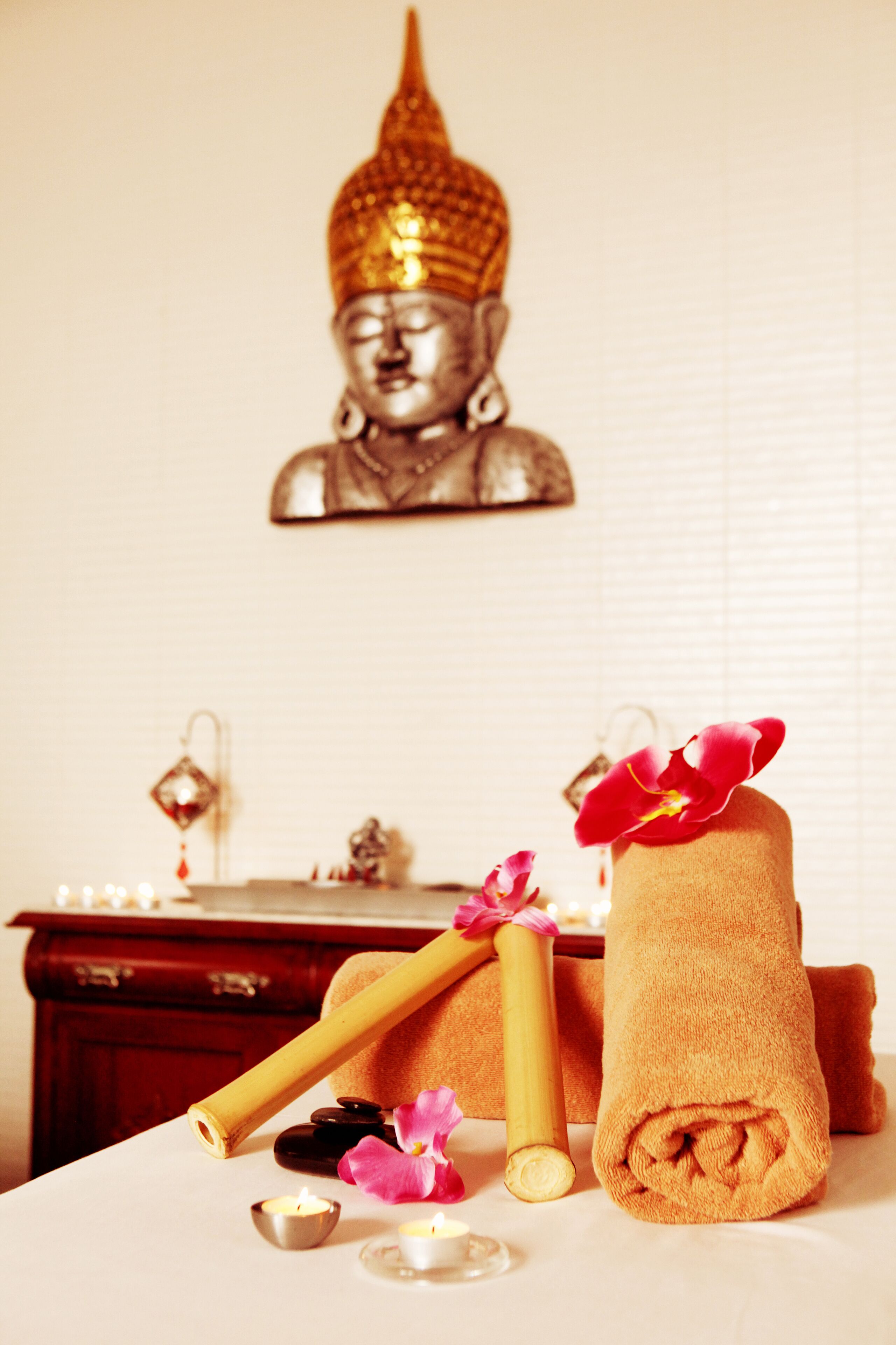 Un ambiente de spa con una estatua de Buda, toallas, velas y flores sobre una mesa.