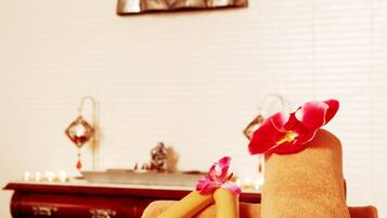 Un ambiente de spa con una estatua de Buda, toallas, velas y flores sobre una mesa.