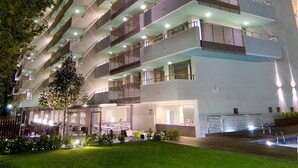 A multi-story hotel with a modern design, featuring balconies on each floor and a well-lit facade.