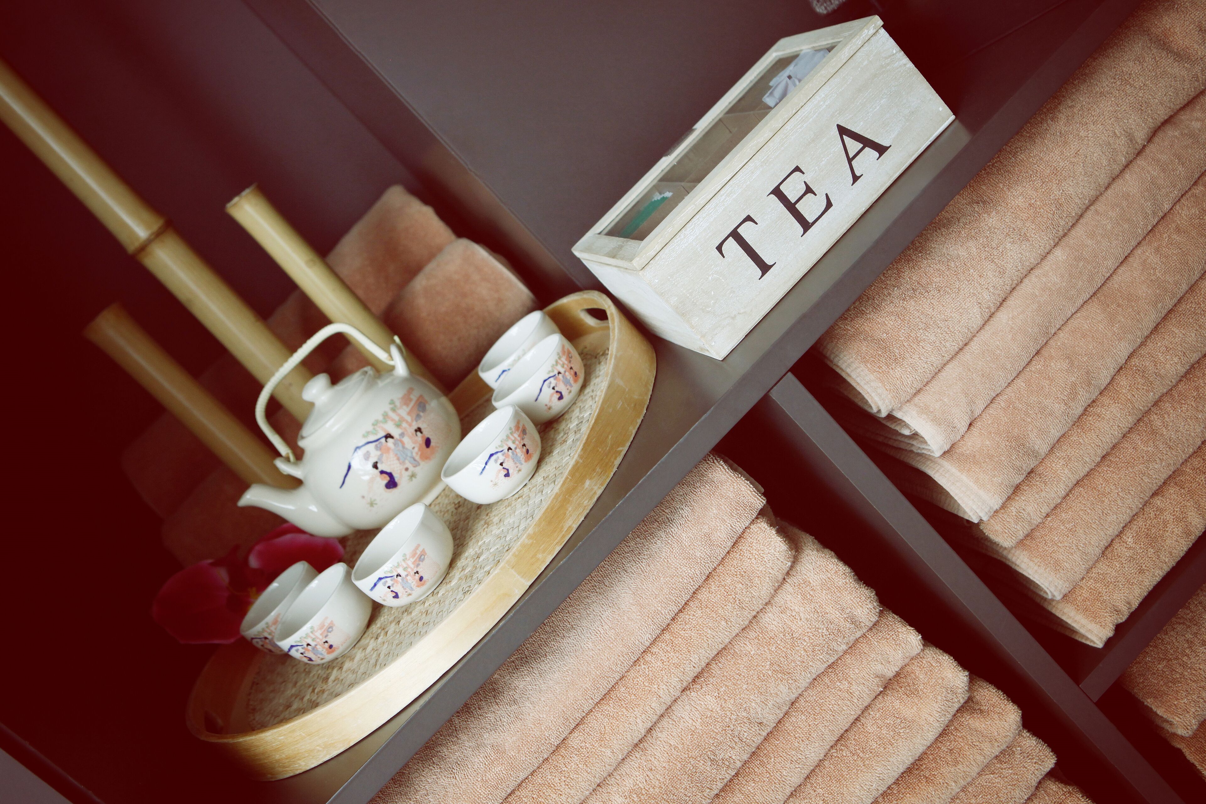 A tea set on a tray with a box labeled "TEA" and towels on a shelf.