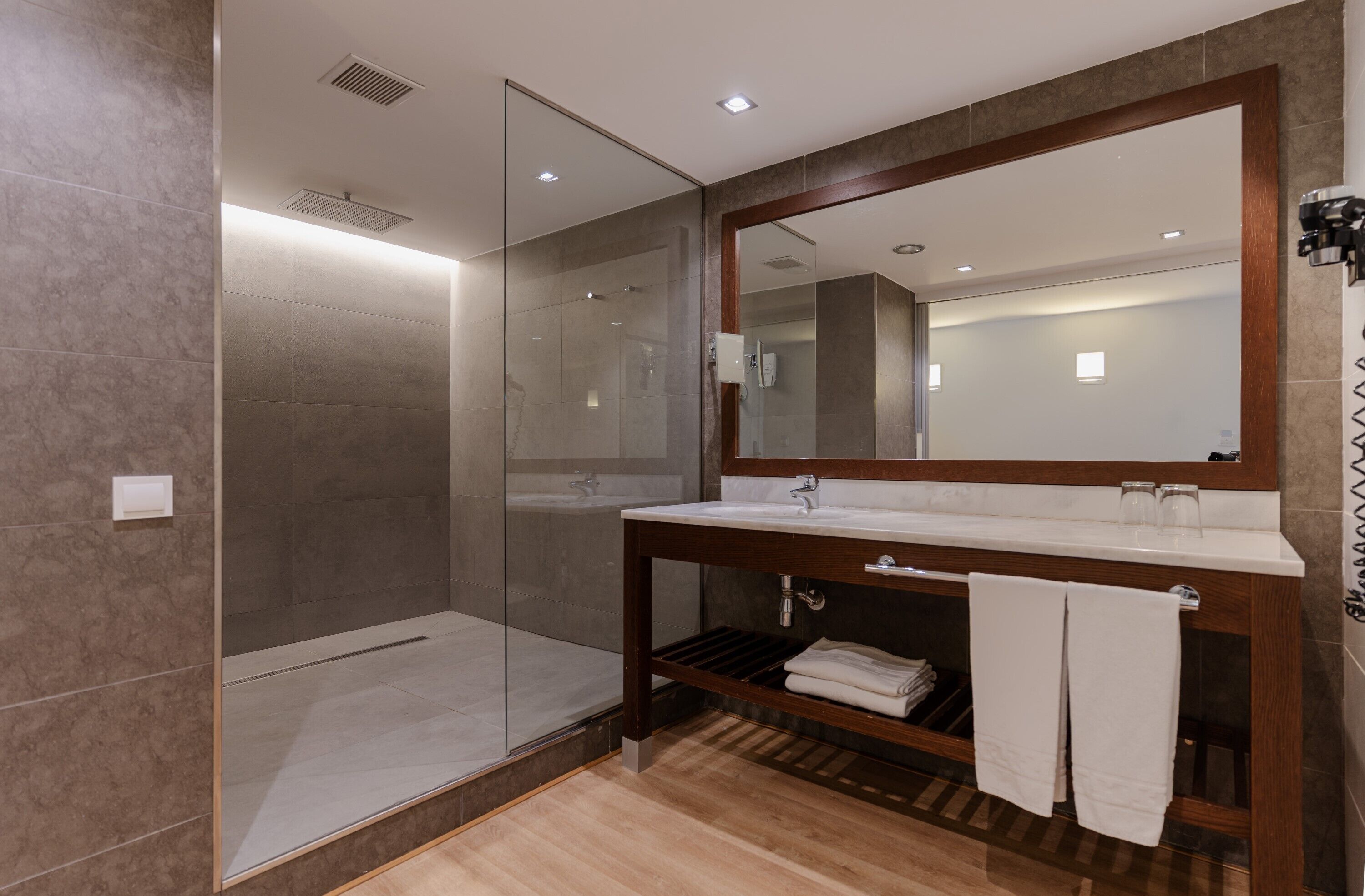 Un baño moderno con ducha envuelta en vidrio, tocador de madera con espejo y perchero.