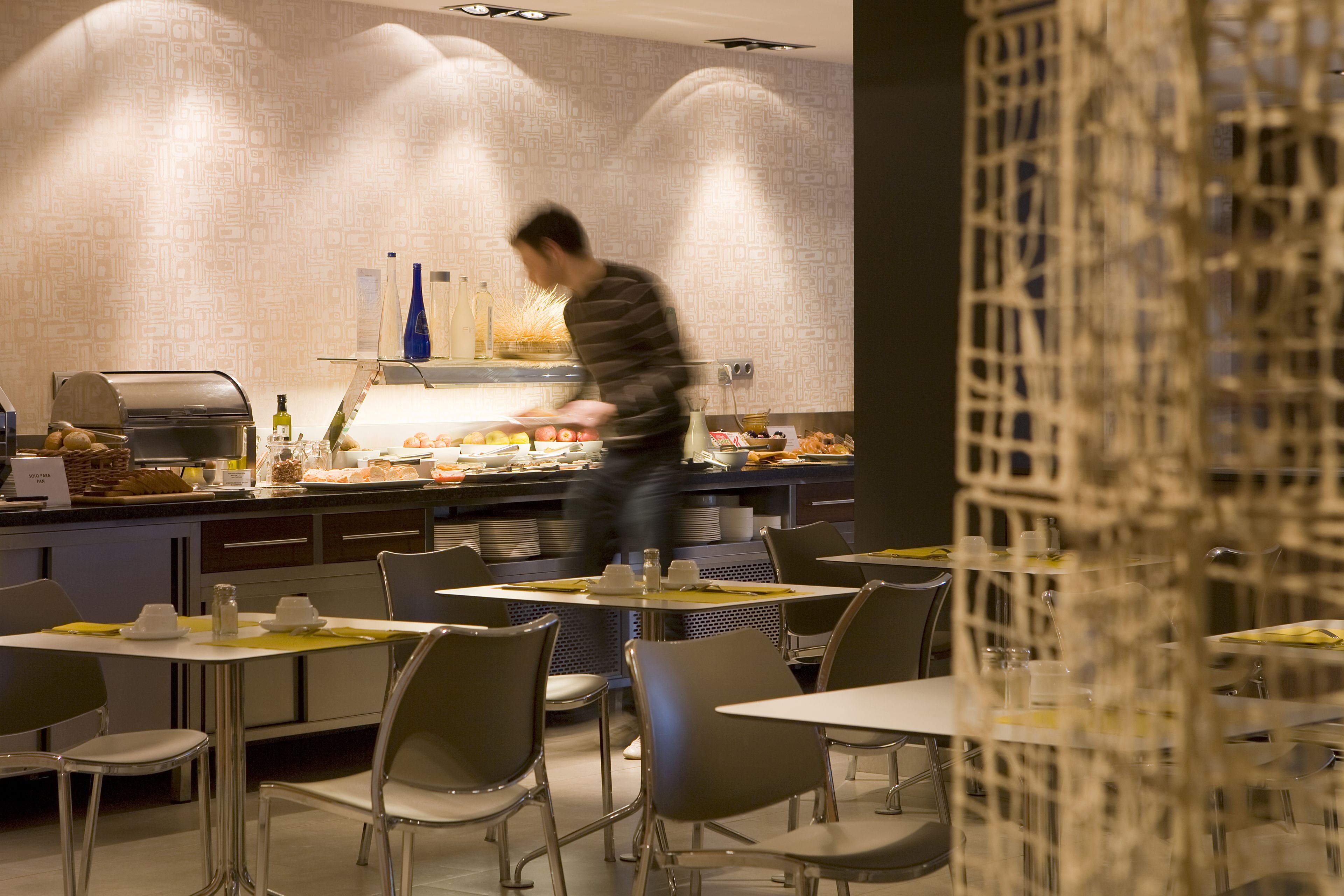 Interior moderno de restaurante con barra de buffet, sillas de metal y pared con diseño.