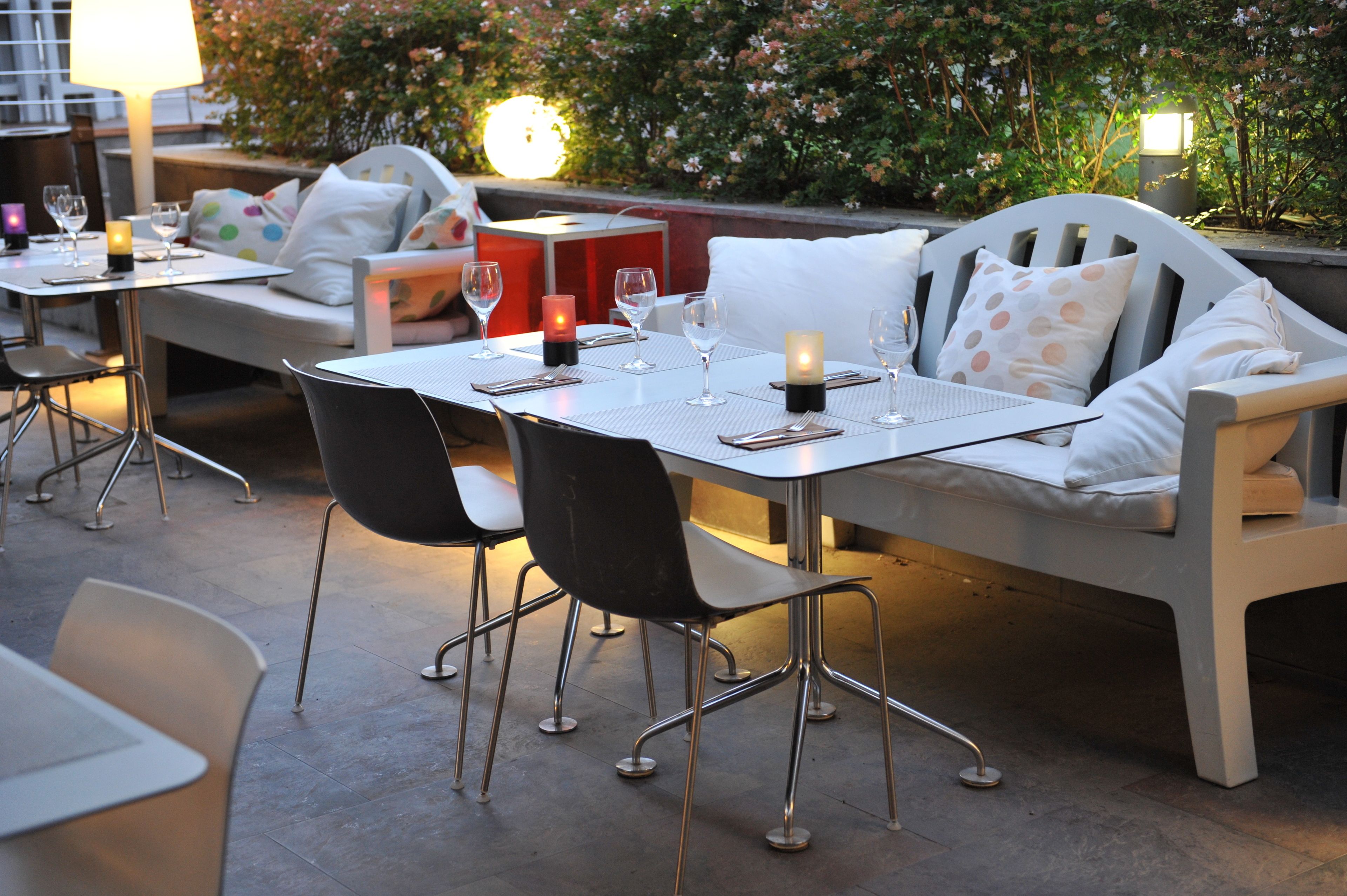 Un espacio al aire libre para comer con mesas, sillas, velas y un banco con almohadones.