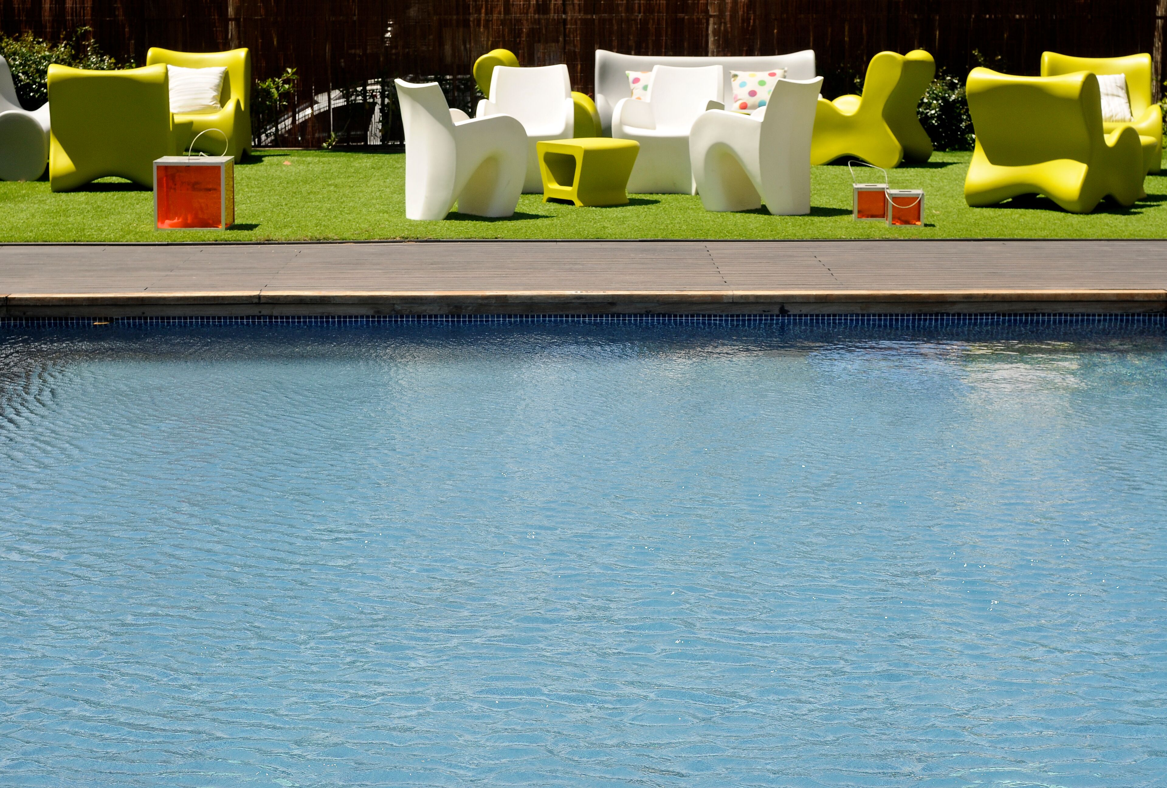 A swimming pool with white and yellow lounge chairs and a small orange container.