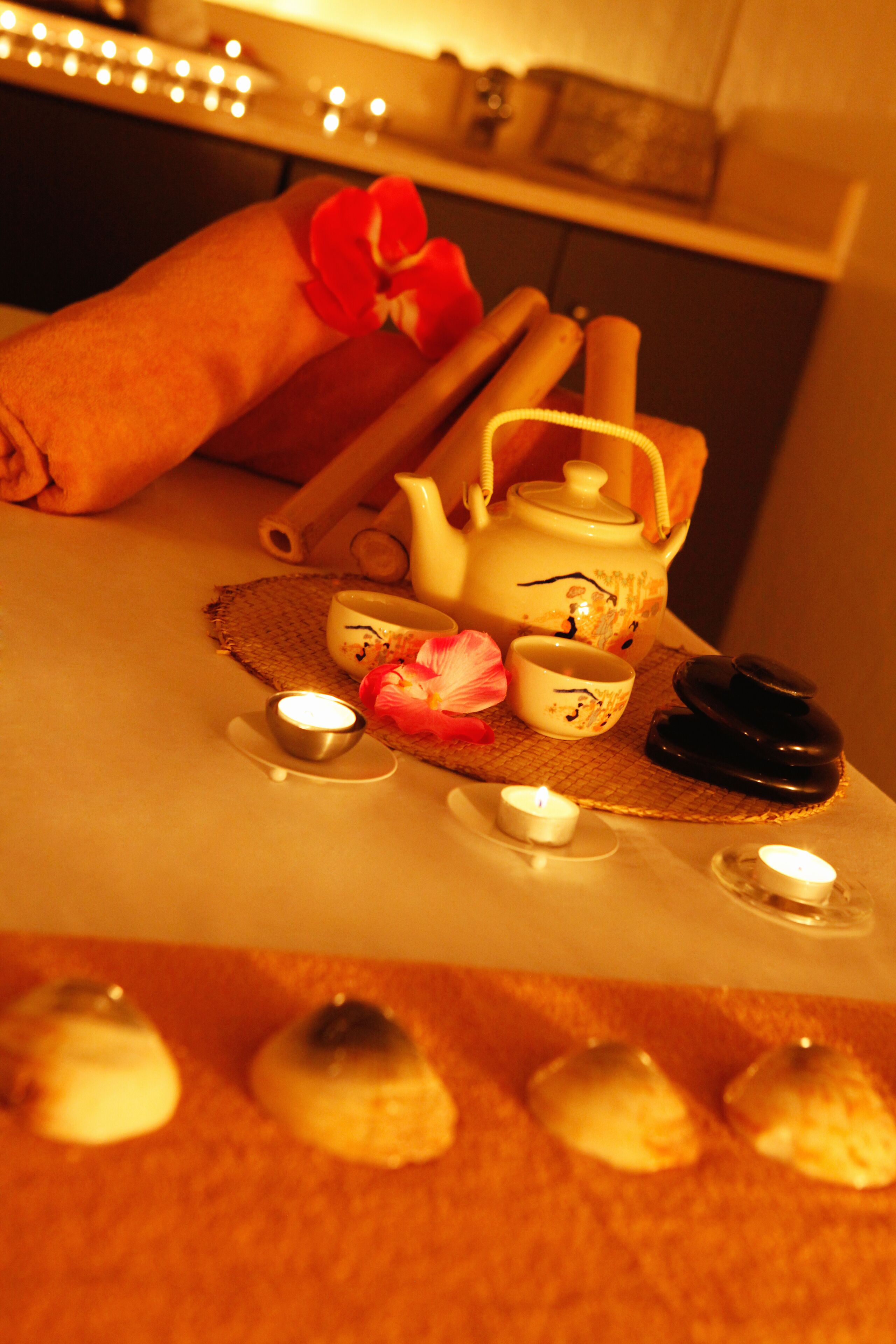 A table with a teapot, cups, a candle, and a flower.