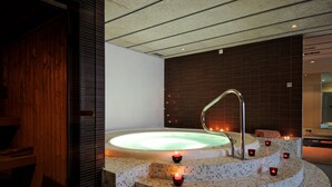 A hot tub with a tiled platform and candles, surrounded by a wooden wall and a modern ceiling.