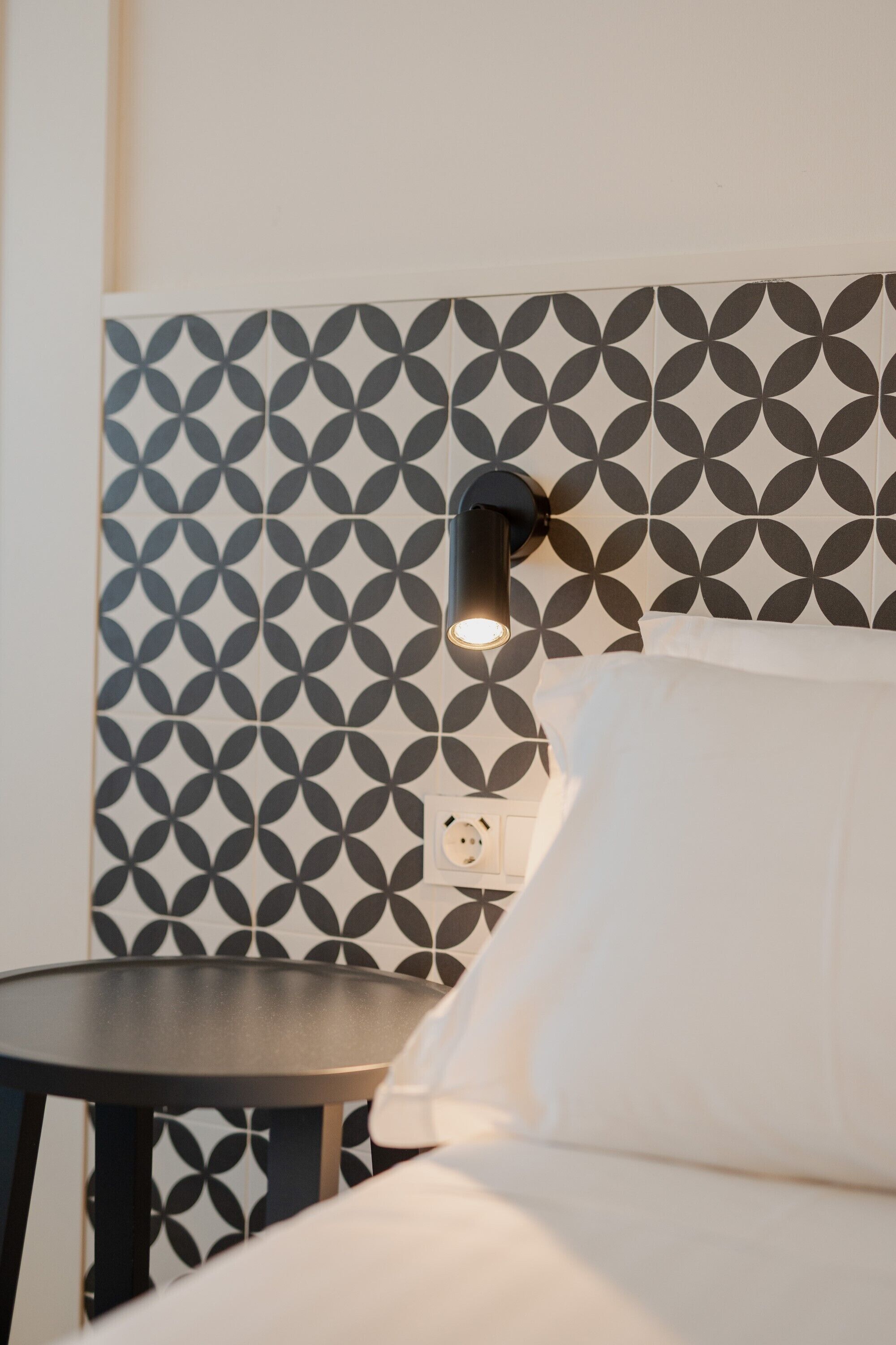 Une chambre d’hôtel avec un mur orné de motifs, une table de chevet et une lampe.
