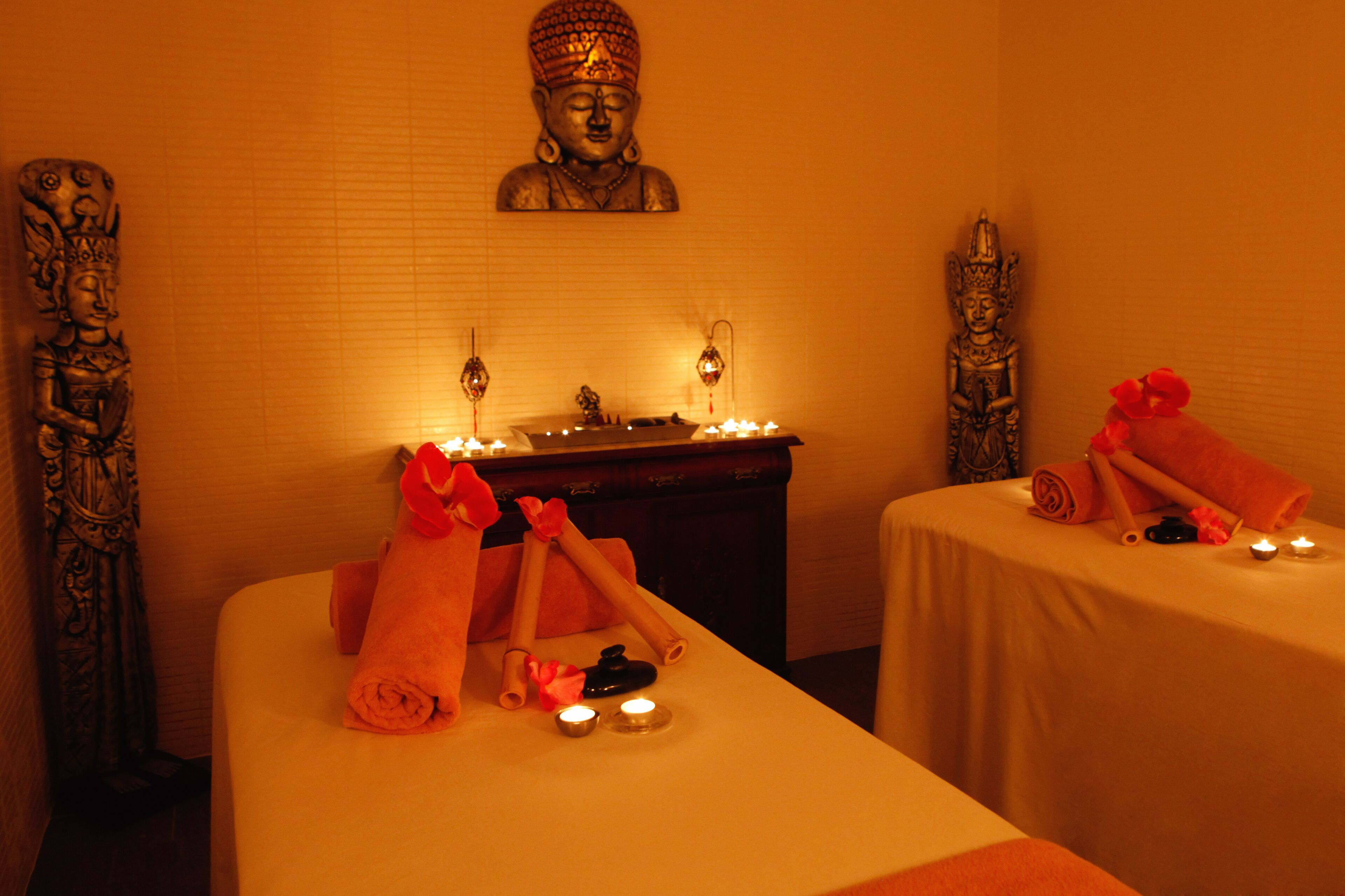 A spa room with two beds, candles, and statues.