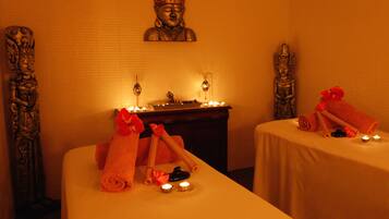 A spa room with two beds, candles, and statues.