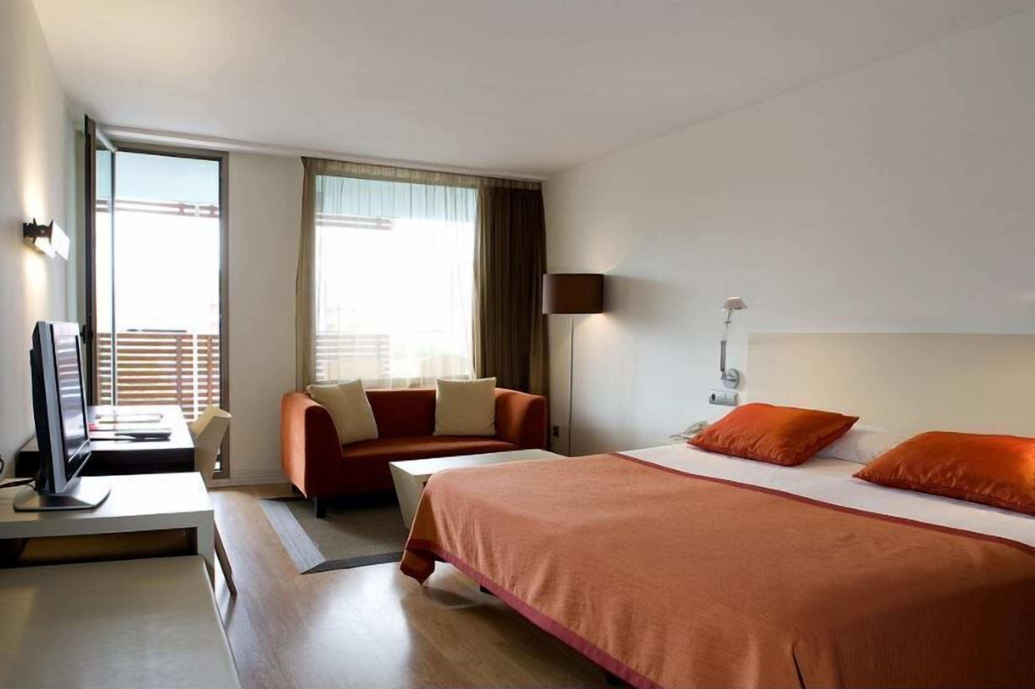 Een hotelkamer met een bed, een bank, een bureau met een computer en een televisie.