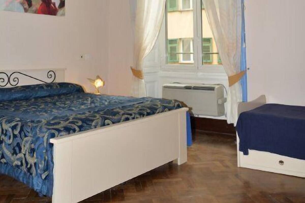 Un dormitorio con una cama grande, una cama más pequeña, una ventana con cortinas y un techo con frescos.