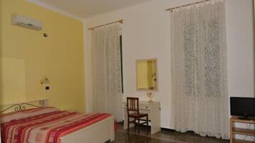 A bedroom with a bed, a desk, a chair, a television, and curtains.