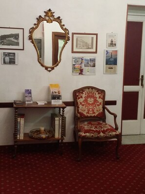 A room with a wooden chair, a mirror, and a shelf with books and a candle. - Balbi Hotel (Genoa)