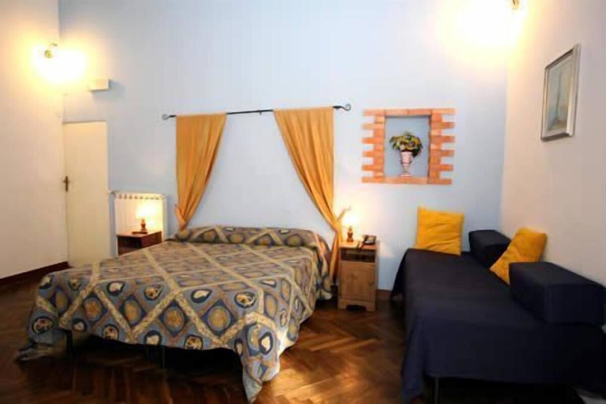 Un dormitorio con cama, mesitas de noche, una repisa en la pared y una ventana pequeña.