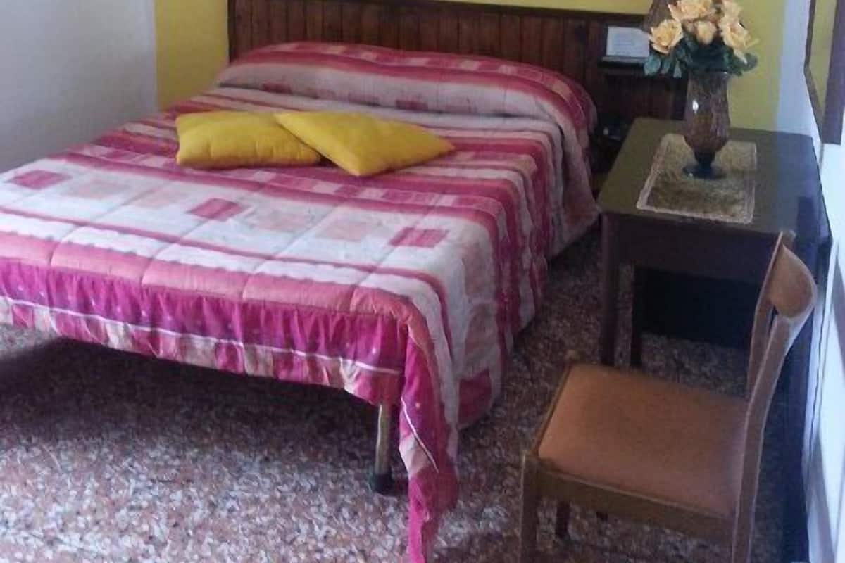 Un dormitorio con cama, una silla, un escritorio y un cuadro en la pared.