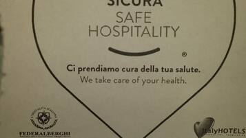 Une pancarte avec les inscriptions « Accoglienza Sicura Safe Hospitality » et « Nous veillons à votre santé ». Elle comporte les logos de « Federalferghi » et « ItalyHotels ».