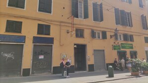 Un bâtiment jaune avec de nombreuses fenêtres et volets, une enseigne indiquant « Hôtel Balbi » et une devanture de magasin nommée « La Focaccia ».