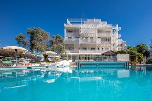 A modern hotel with a swimming pool, multiple balconies, and a clear blue sky.
