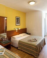 Quarto de hotel com cama, mesa de cabeceira, luminária e um quadro na parede.