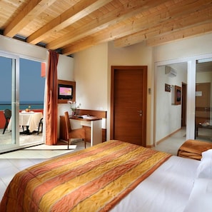Habitación de hotel con cama, escritorio, silla, televisor y puerta corrediza de cristal que da a un balcón.