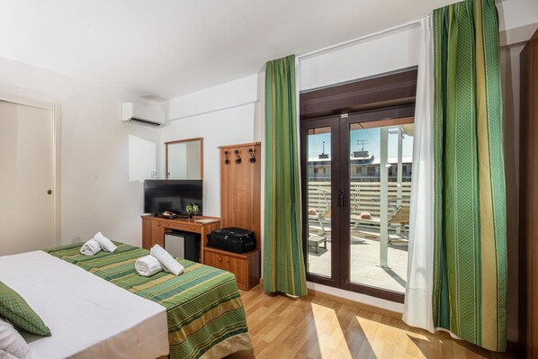 Une chambre d’hôtel comprenant un lit, un bureau, une télévision, une armoire et une porte-fenêtre coulissante donnant sur un espace extérieur.
