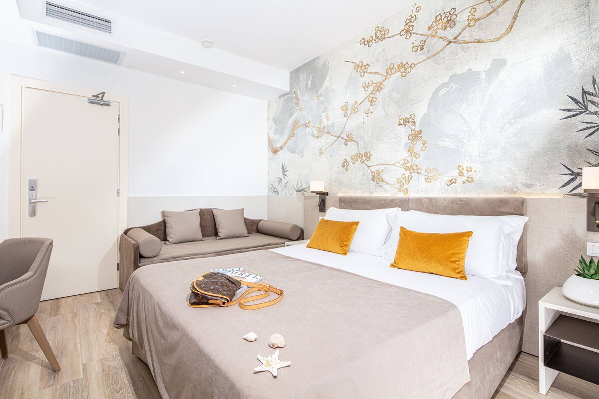 Une chambre d’hôtel avec un lit, une chaise, une table de chevet et un mur orné d’une fresque florale.