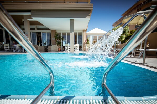 A swimming pool with clear blue water, surrounded by lounge chairs and umbrellas, and a building with large windows in the background.