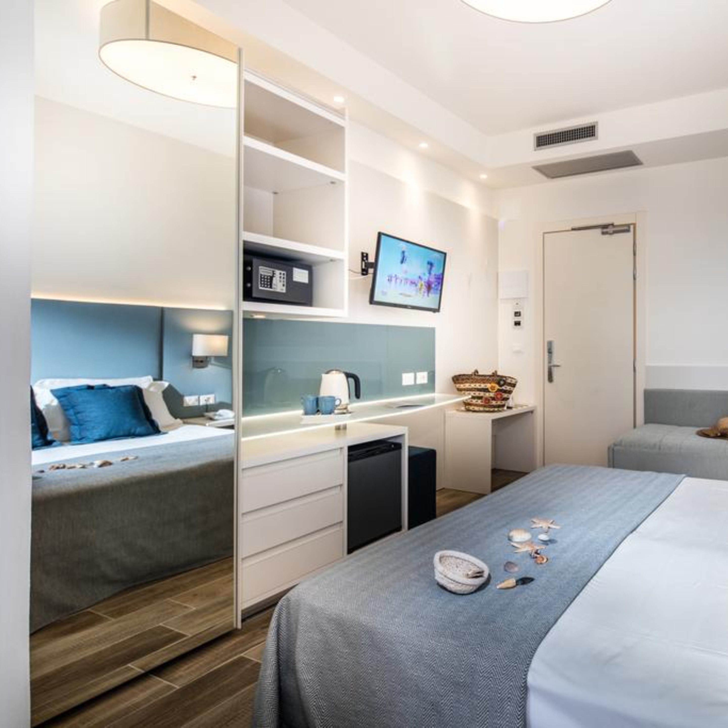 A modern hotel room with a bed, a desk, a television, and a wardrobe.