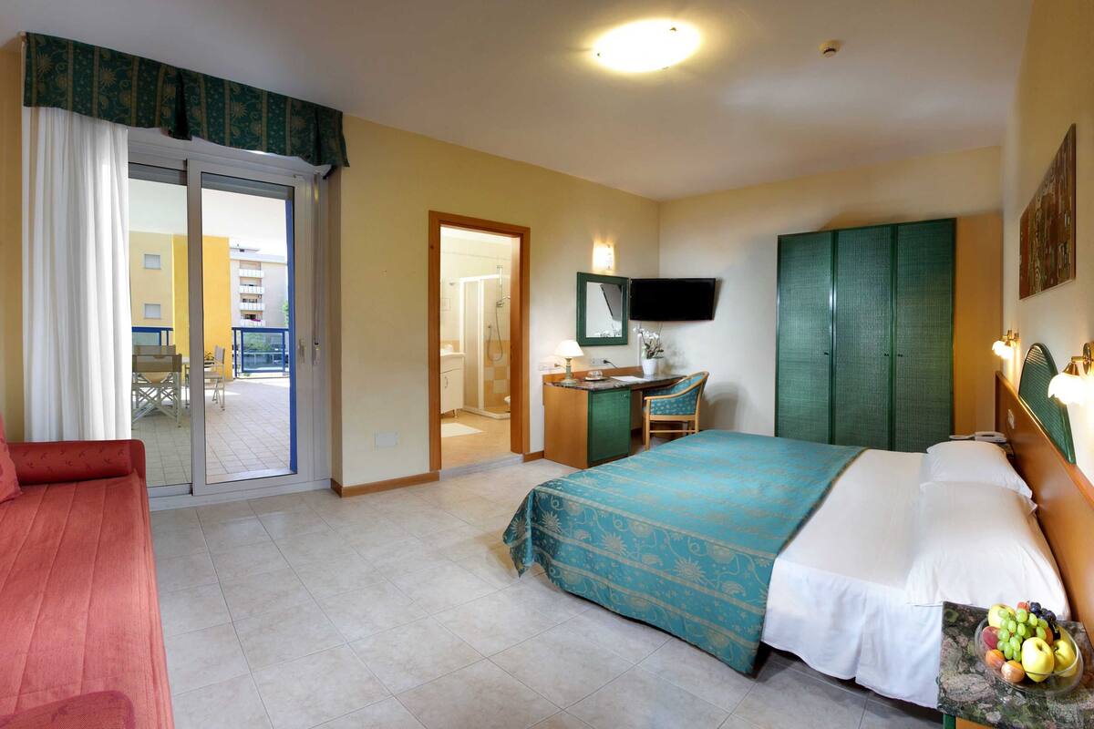 Een hotelkamer met een bed, bureau, stoel, televisie en balkon.