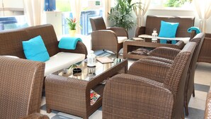 A wicker lounge area with a glass coffee table, blue cushions, and a potted plant. - Hotel Bellevue (San Michele al Tagliamento)
