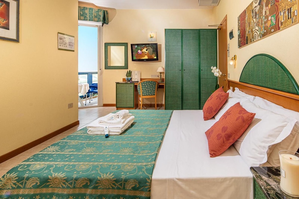 Ein Hotelzimmer mit Bett, Schreibtisch, Stuhl und einer grünen Tür.