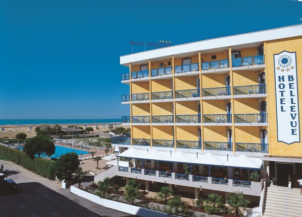 A multi-story hotel with balconies, a pool, and a beach view.